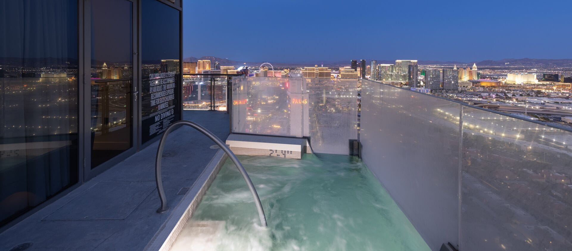 Une piscine sur le toit offrant une vue sur la ville, une barrière en verre et un panneau indiquant les consignes de sécurité.