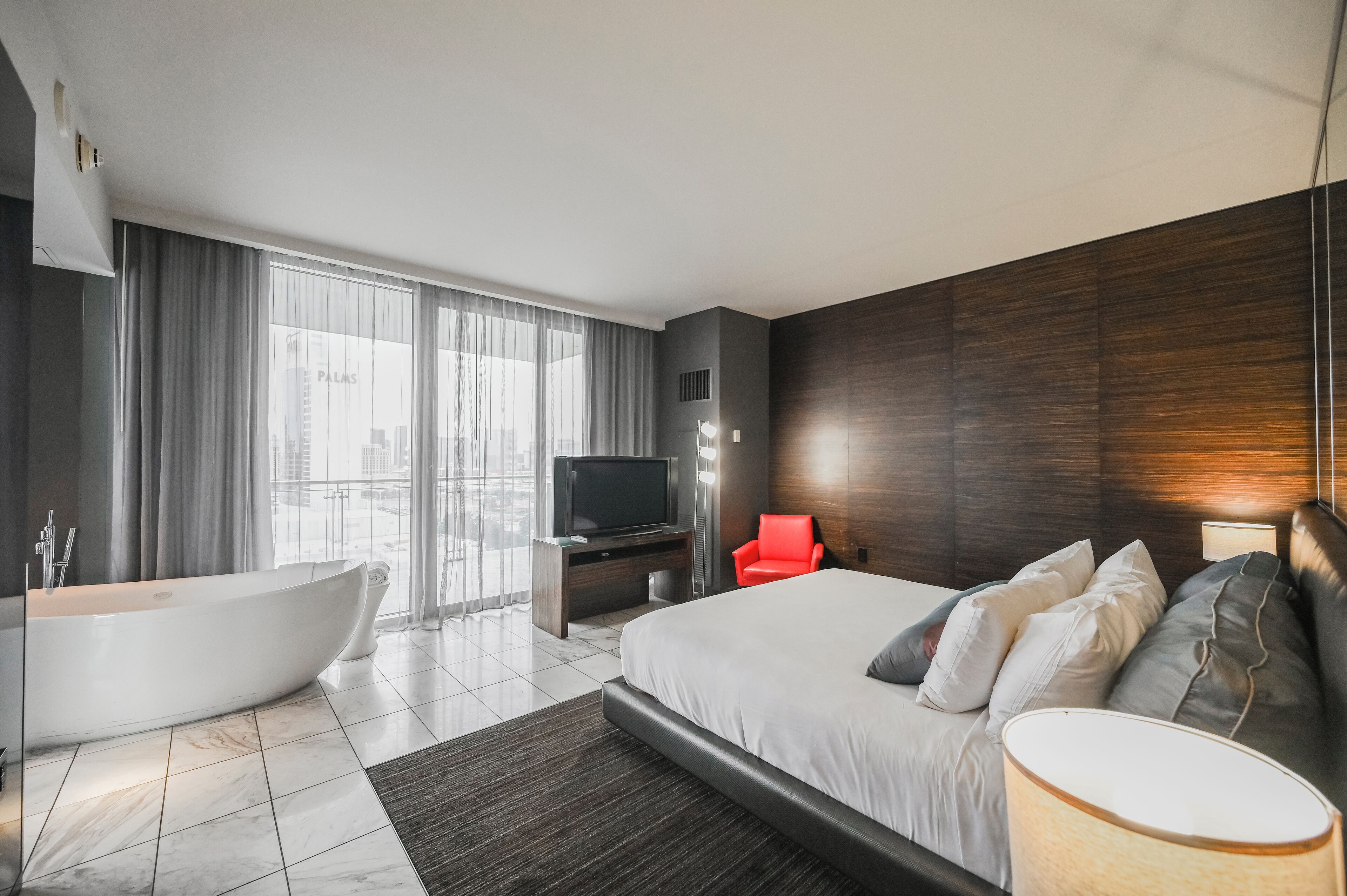 Ein modernes Hotelzimmer mit einem großen Bett, einer Badewanne, einem Flachbildfernseher und Blick auf die Stadt.