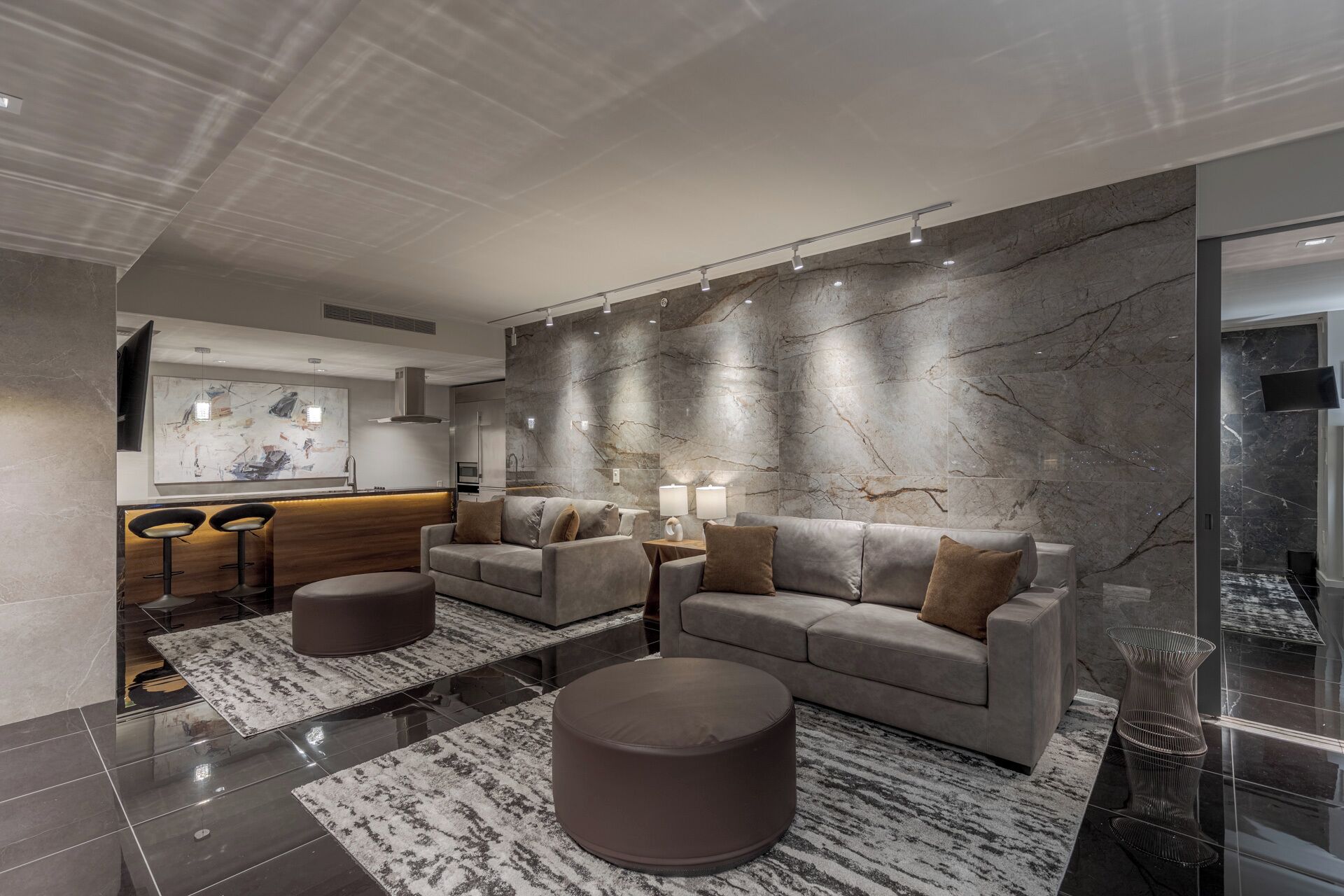 A modern living room with a grey sofa, two ottomans, a coffee table, and a bar area with stools.