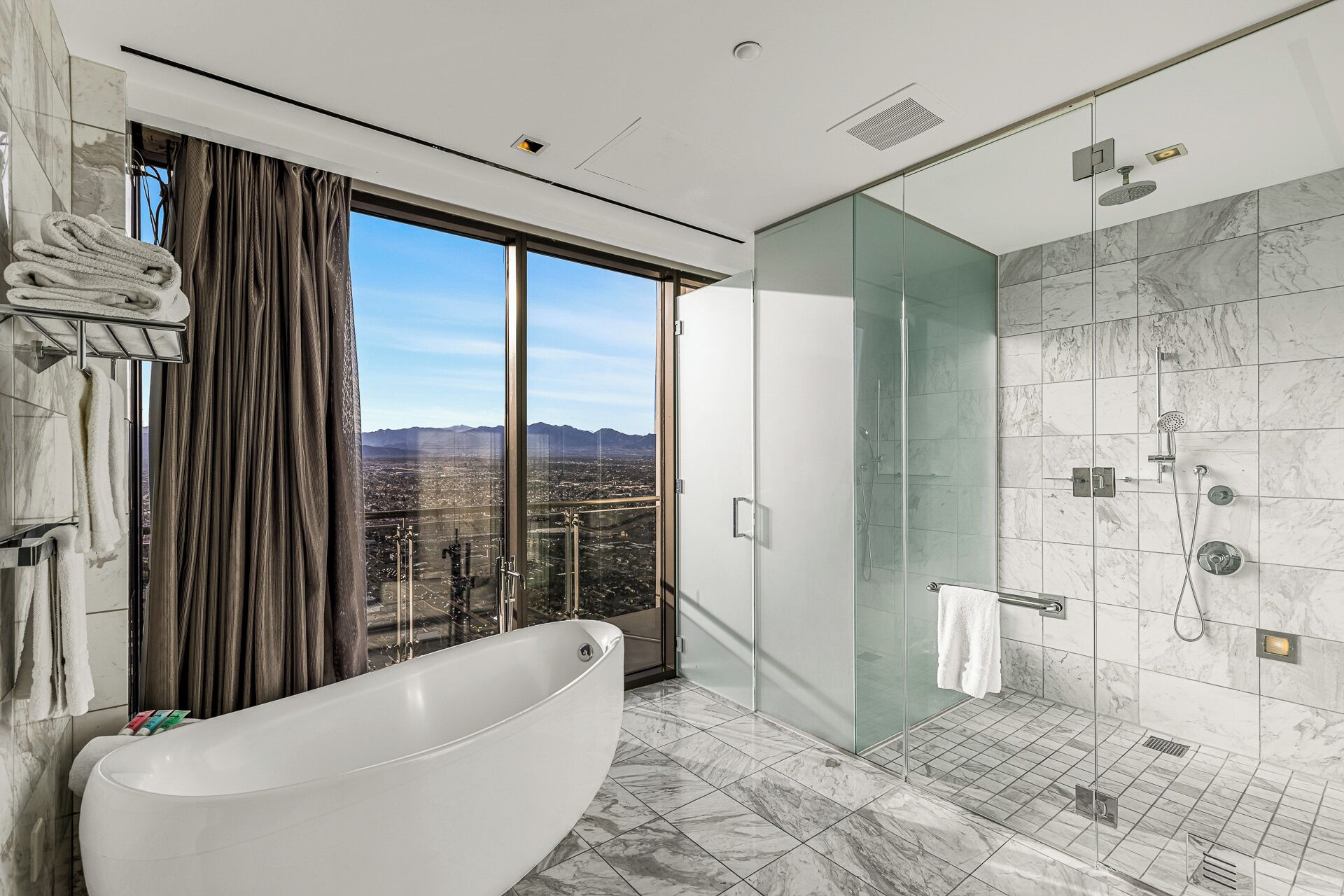 A modern bathroom with a freestanding bathtub, a glass-enclosed shower, and a city view.