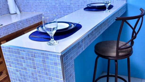 Een bar met een blauw betegelde toonbank, twee krukken en een glas water.