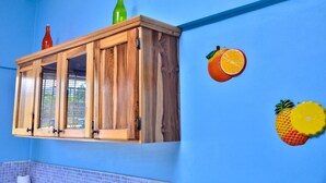 Een houten kast met glazen deuren, tegen een blauwe muur, met een groene fles erop en fruitdecoraties.