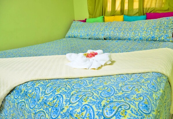A bed with blue and yellow patterned bedding, a white towel with a flower, and colorful pillows. - Kingston Sunset Guest Apartment II (Kingston)