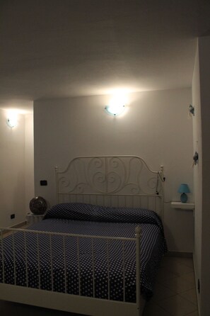 Ein Schlafzimmer mit einem Metallbettgestell, einer Betttdecke mit Punkten und zwei Wandleuchten.