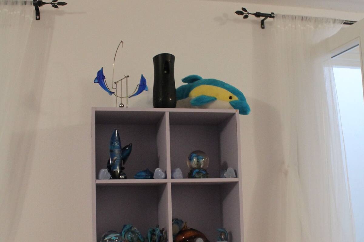 Une étagère blanche ornée d’objets décoratifs, notamment un poisson bleu, un vase noir et divers objets en verre.