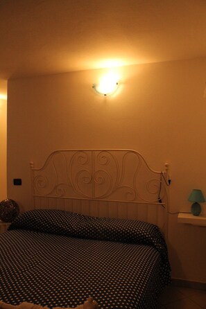 Ein Schlafzimmer mit einem Bett, einer Wandleuchte und einem kleinen Regal mit einer Lampe.