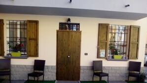 A building entrance with a wooden door, two windows with shutters, and two chairs outside.