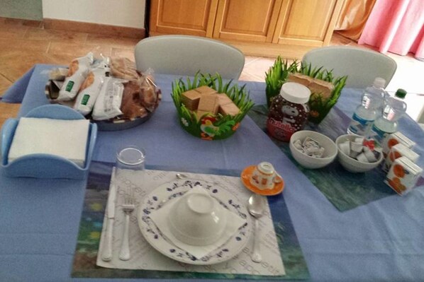 A dining table set with a white plate, a cup, a glass, and a napkin. There are also bags of snacks, a jar of jam, and a bottle of water on the table. - B&B Il Delfino a Bologna (Bologna)