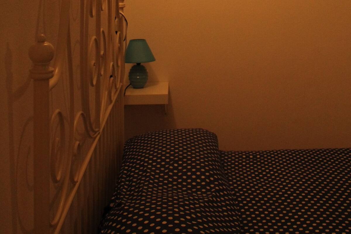 Une chambre à coucher comprenant un lit, une table de chevet, une lampe et deux décorations en forme de cœur fixées au mur.