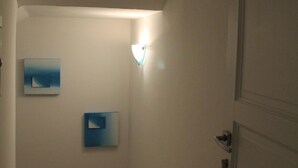 A narrow hallway with white walls and a door on the right. There are two framed pictures on the wall.