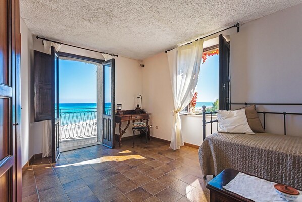 Un dormitorio con cama, escritorio, silla y vista al mar a través de una puerta abierta.