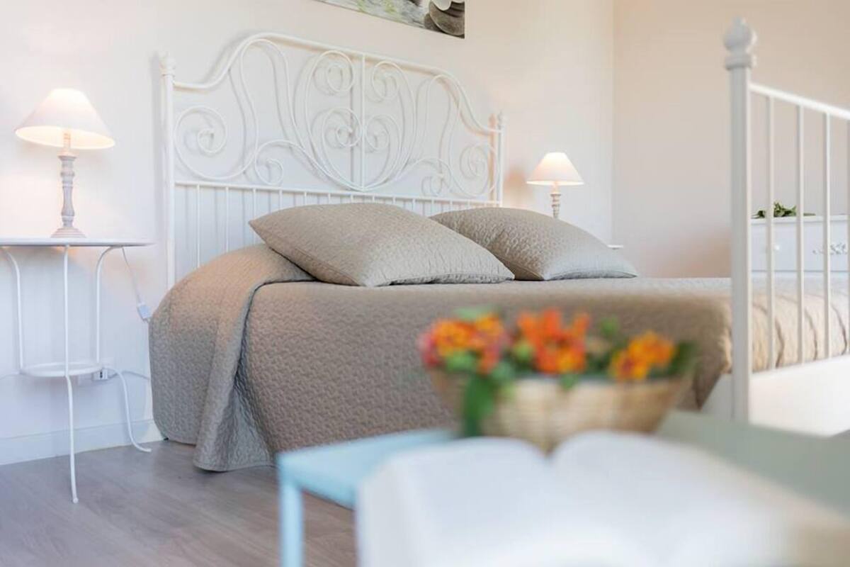 A neatly arranged bedroom with a white metal headboard, a beige bedspread, and two bedside lamps.