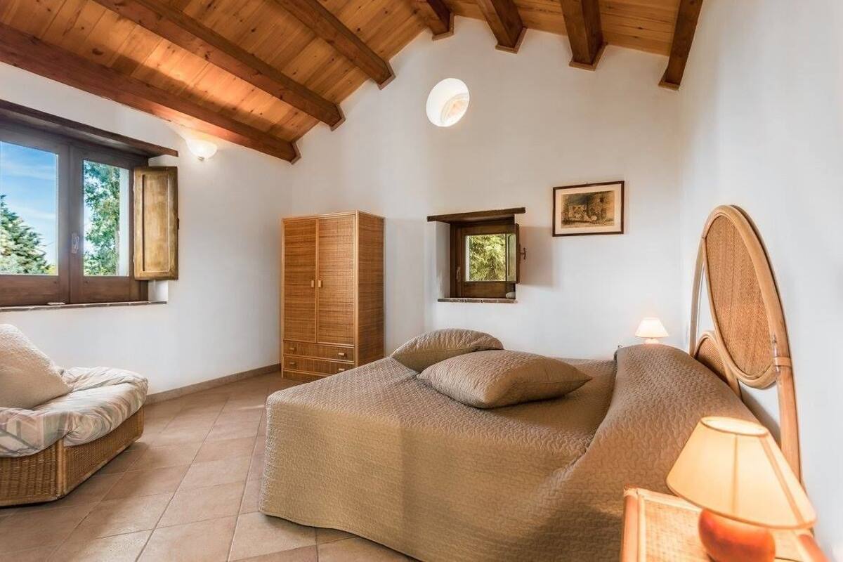 A bedroom with a bed, a chair, a wardrobe, and a window.