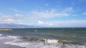 A beach with waves, a clear sky, and distant mountains. - Sunrise Villa On The Beach (Portmore)
