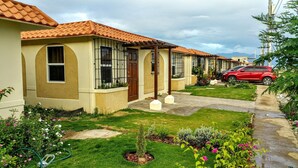 A row of houses with tiled roofs, a red car parked in front, and a well-maintained garden with various plants and flowers. - Sunrise Villa On The Beach (Portmore)