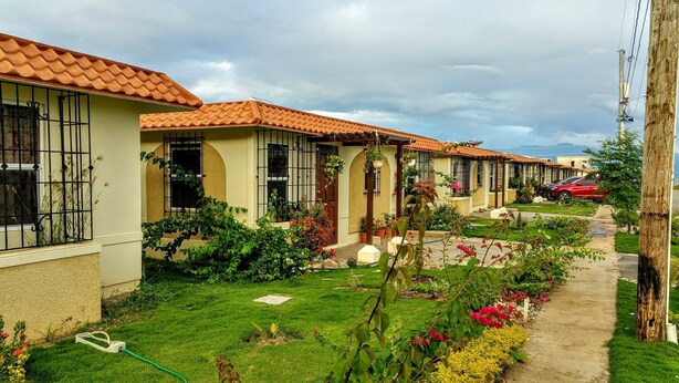 A row of single-story houses with tiled roofs, a well-maintained garden, and a clear sky. - Sunrise Villa On The Beach (Portmore)