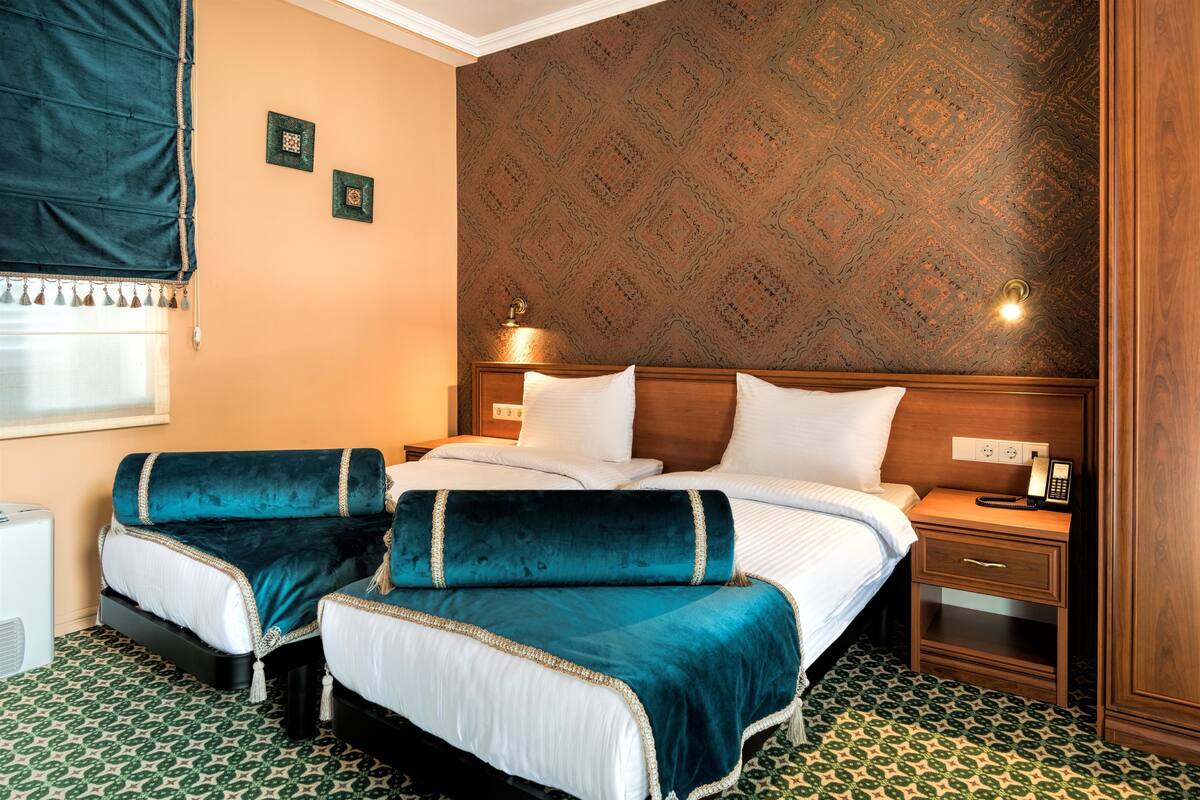 Ein Hotelzimmer mit einem Bett, zwei Nachttischen, einem Schreibtisch, einem Telefon und einem Fenster mit Vorhang.