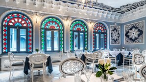 Un comedor con sillas y mesas blancas, amplias ventanas de vitral y elaborados diseños en las paredes.