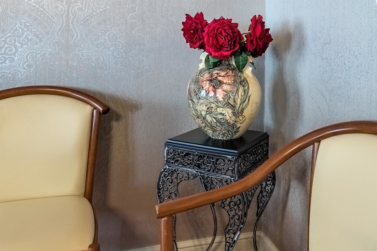 Eine Vase mit roten Blumen auf einem schwarz-weißen Tisch zwischen zwei Holzsesseln.