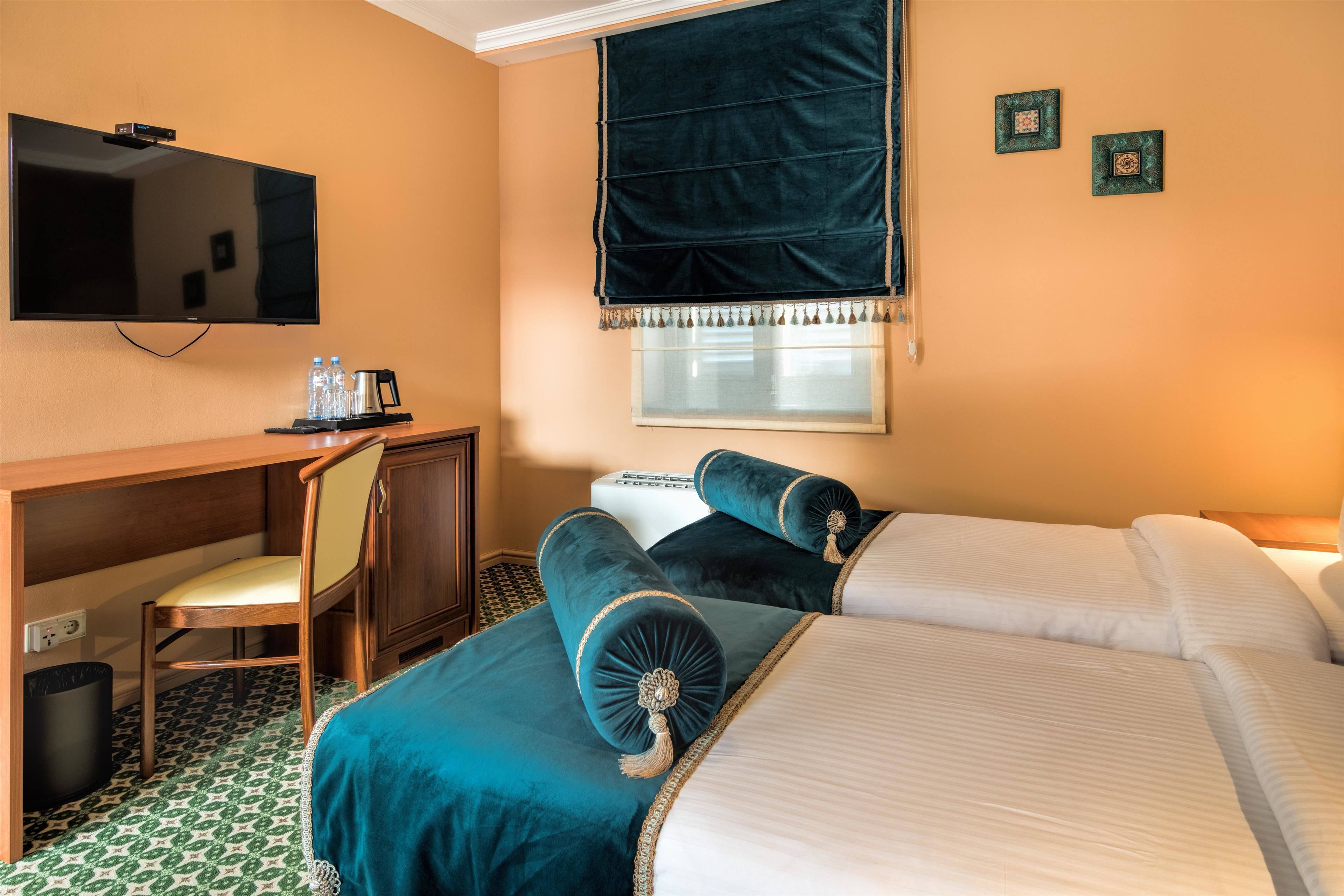 Habitación de hotel con cama, escritorio, silla, televisión y ventana con cortinas.