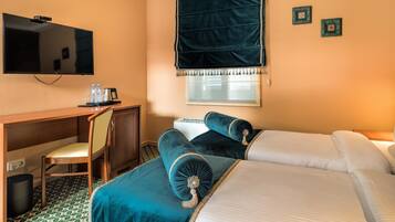 Habitación de hotel con cama, escritorio, silla, televisión y ventana con cortinas.