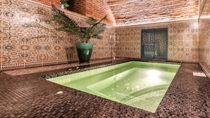 Un área de spa con una piscina climatizada verde, una planta en maceta y elaborados diseños de azulejos en paredes y techo.