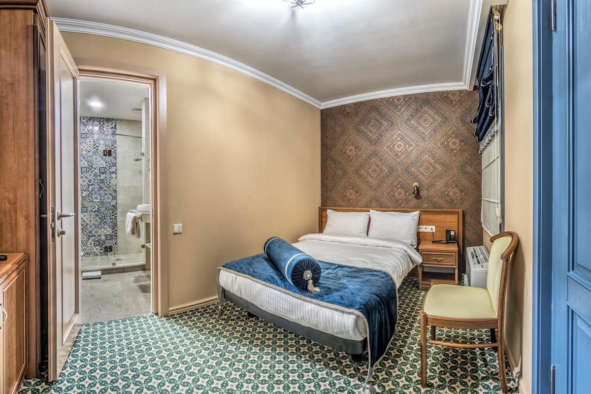 Ein Schlafzimmer mit Bett, Stuhl, Nachttisch und einem Badezimmer mit gemusterten Fliesen.