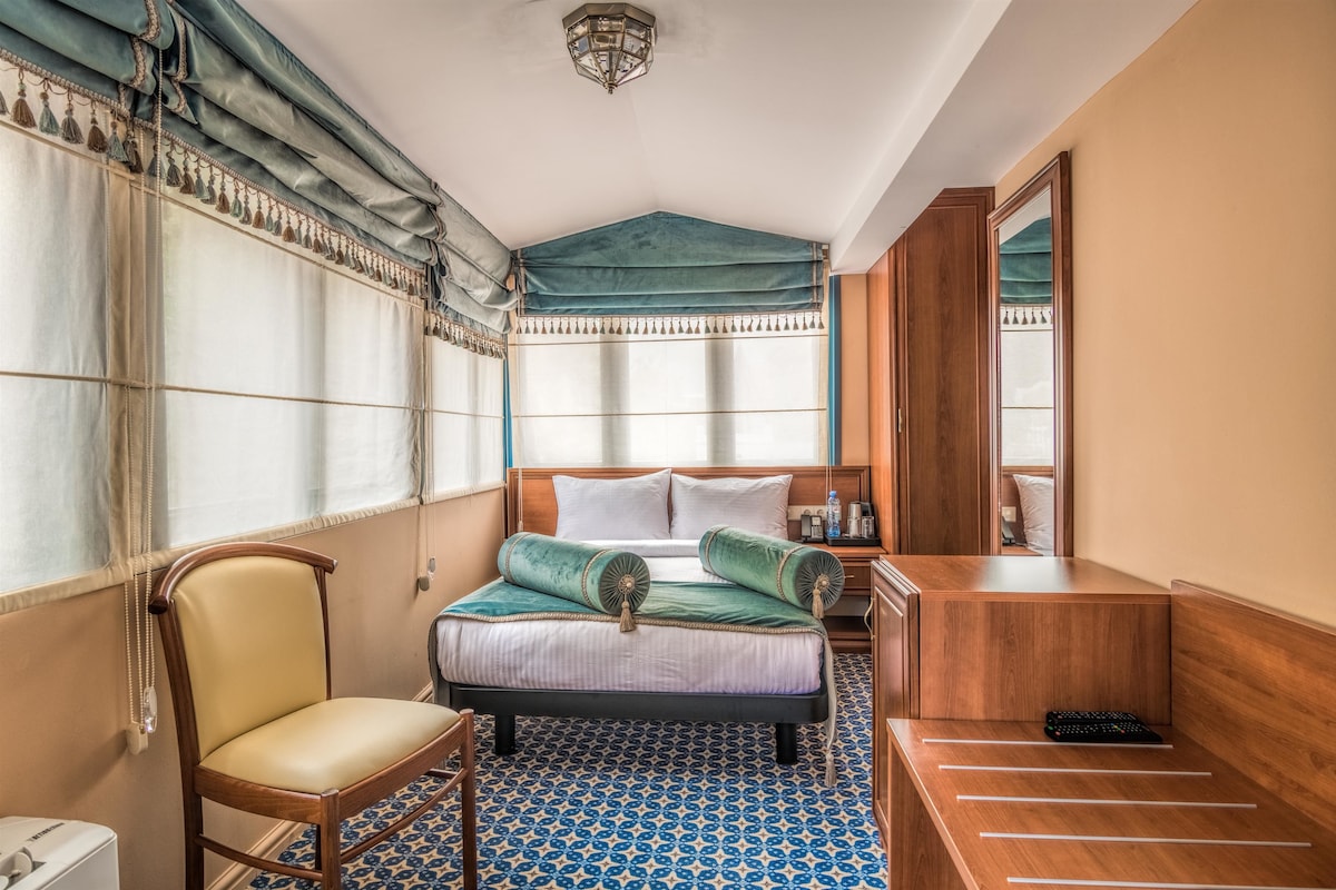 Una habitación de hotel con una cama, una silla, una mesita de noche y un banco de madera.