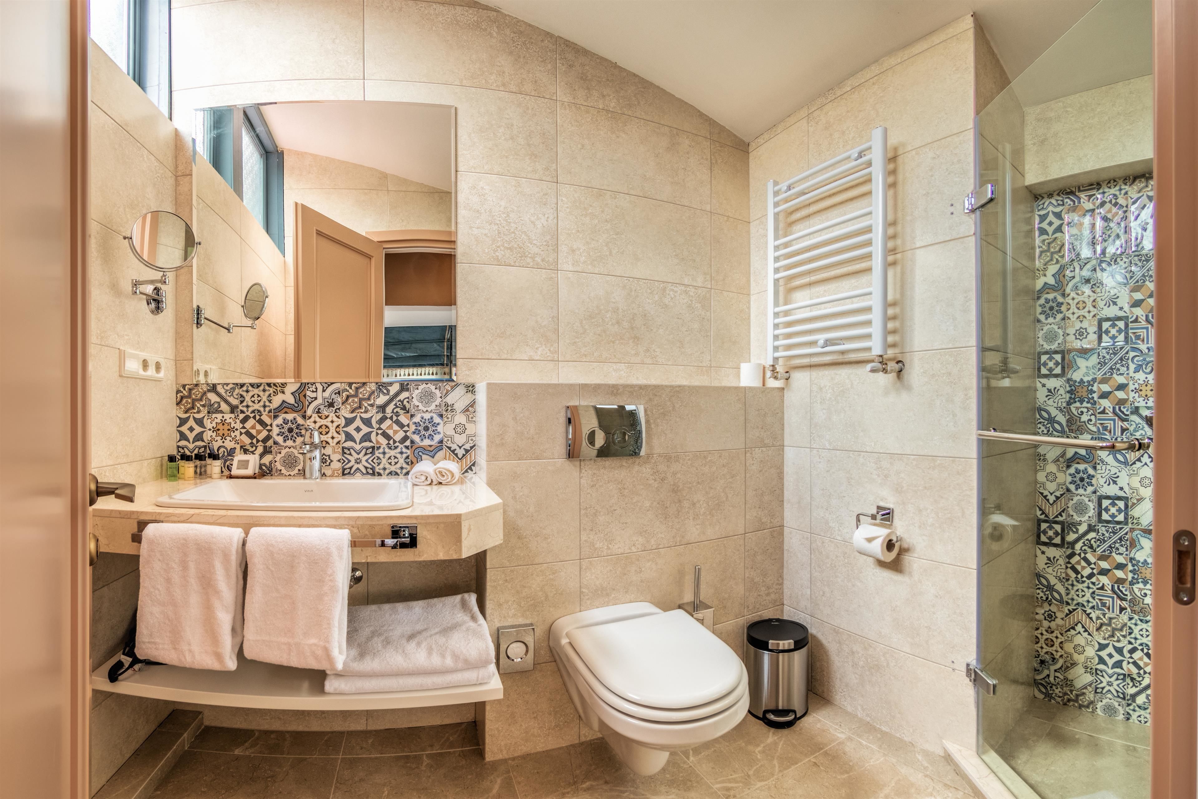 Un baño moderno con un mueble de tocador curvo, un inodoro, una ducha con puerta de vidrio y un salpicadero de azulejos con diseño.