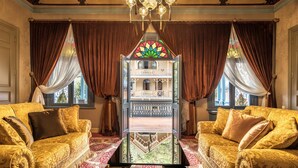 Una habitación lujosa con dos sofás ornamentados, una mesa de centro de vidrio y vistas a un balcón a través de una ventana con vitrales.