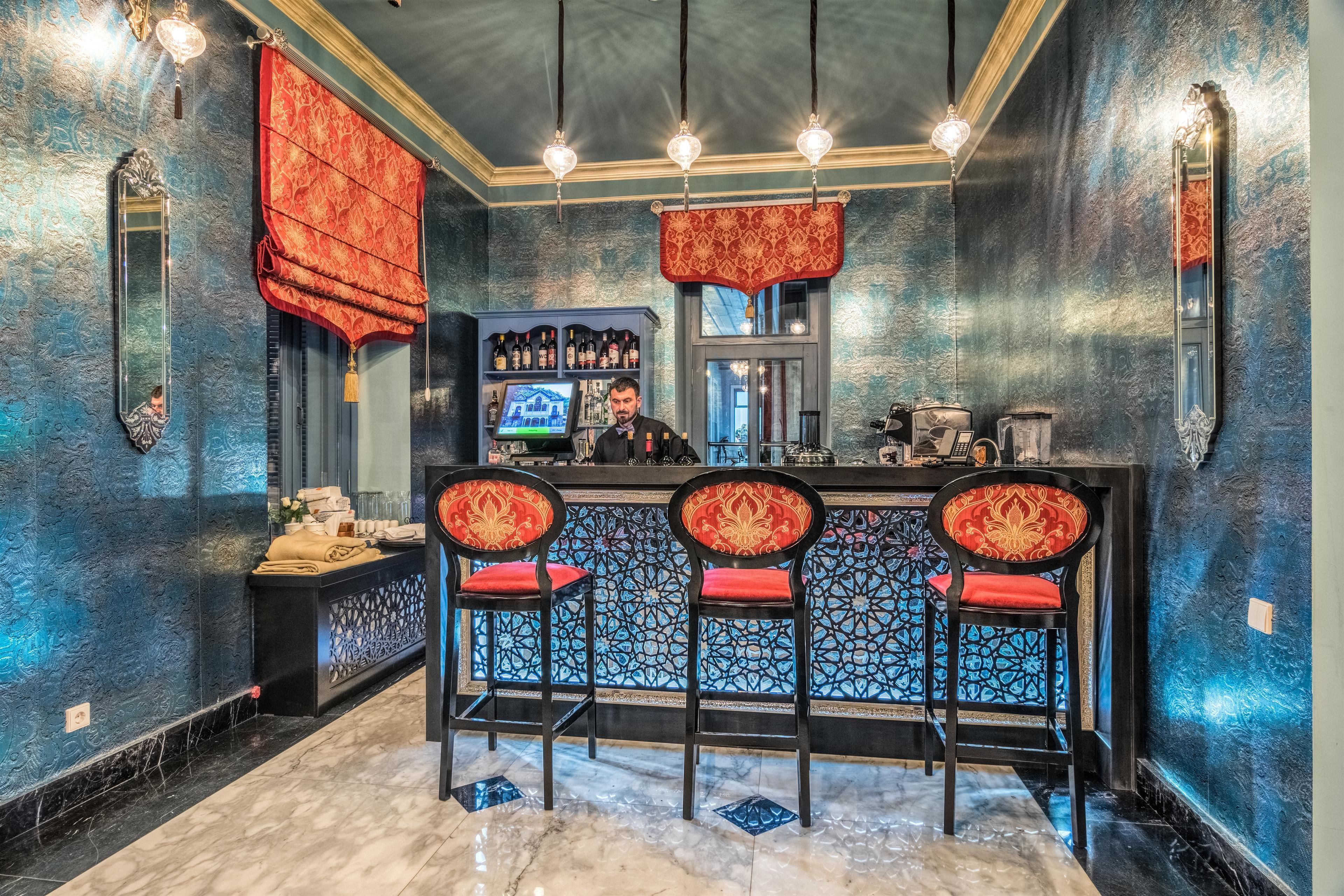 Zona de bar con barra, tres taburetes tapizados en rojo, una pantalla de televisión y una estantería con botellas.