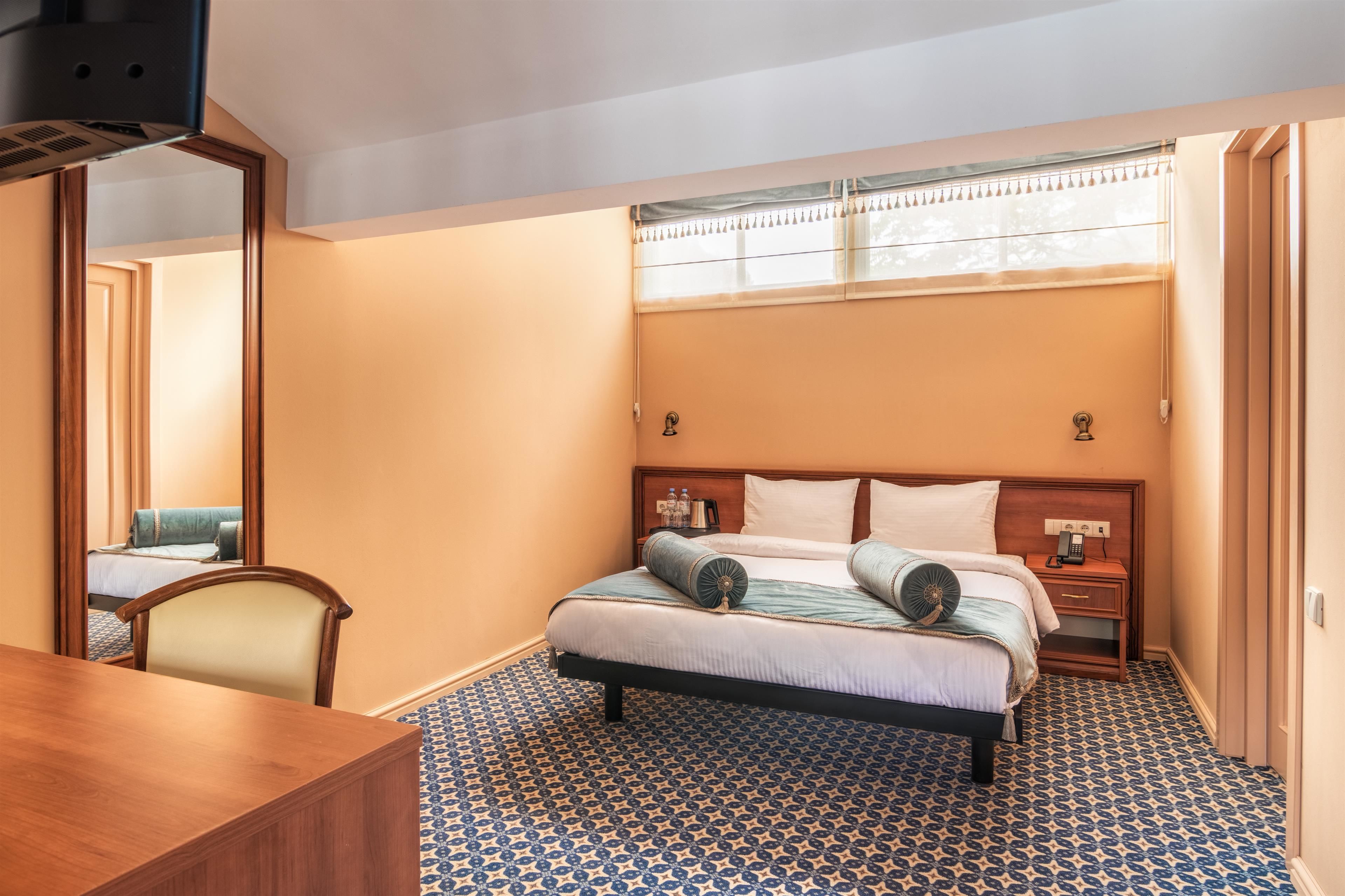 Quarto de hotel com cama, mesa de cabeceira, abajur e espelho.