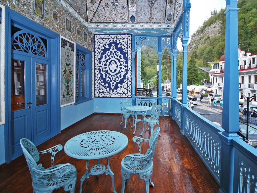 Un balcón azul y blanco decorado con suelo de madera, sillas y mesas de metal.