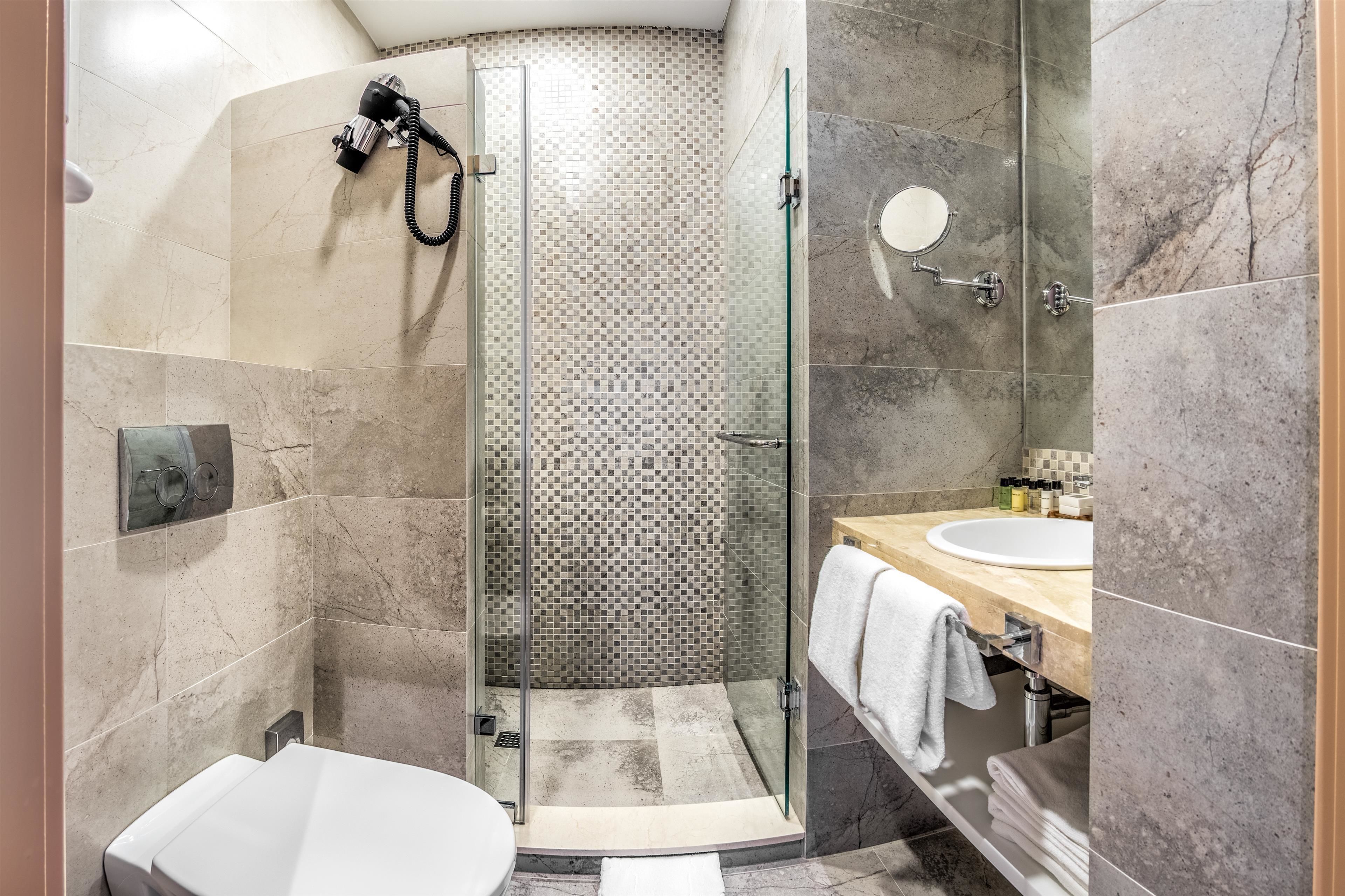 Un baño moderno con ducha acristalada, inodoro blanco y tocador con lavamanos y perchero para toallas.