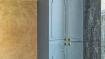 A grey wardrobe with two doors and a shelf, placed against a textured wall with a wooden trim ceiling.