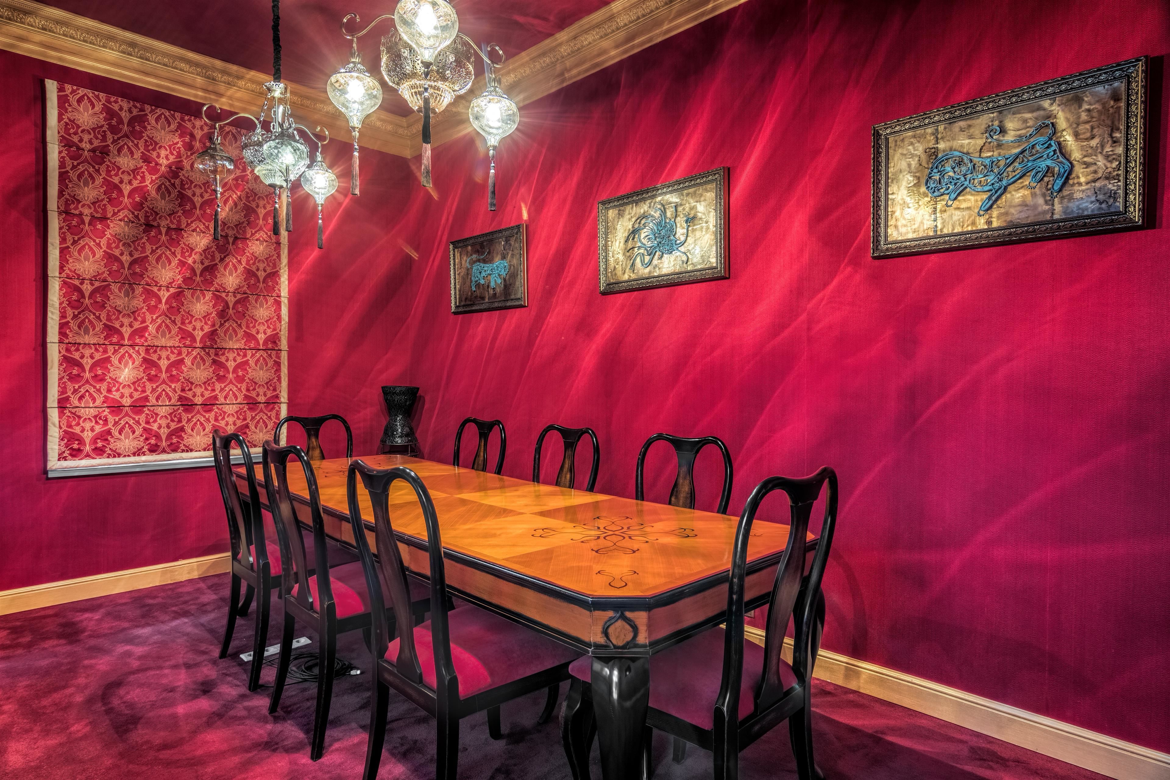 Comedor con una larga mesa de madera, sillas negras y paredes rojas.