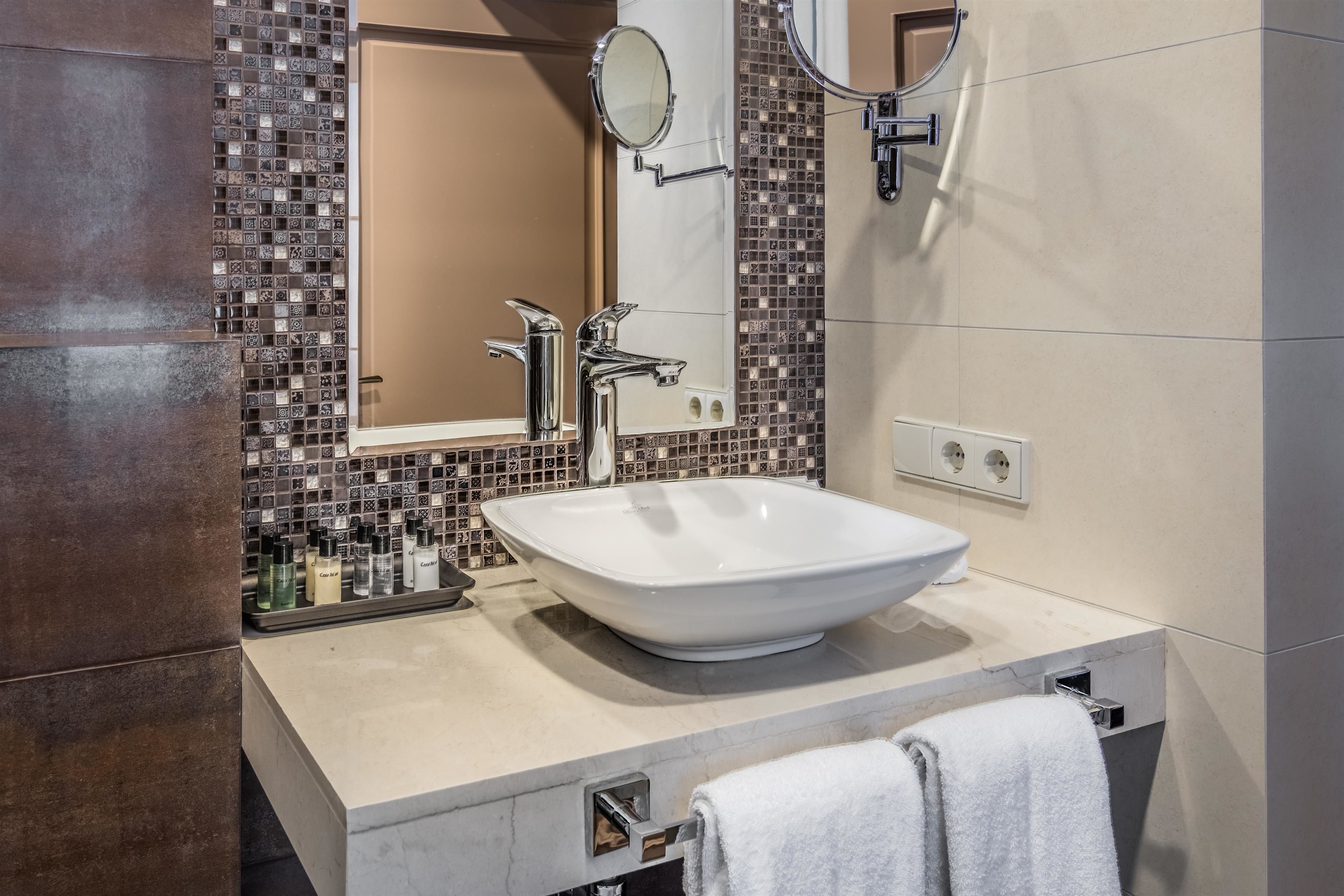 Une salle de bain moderne avec un grand lavabo sur colonne, deux miroirs et un mur recouvert de carreaux.
