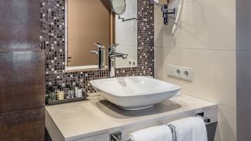 Une salle de bain moderne avec un grand lavabo sur colonne, deux miroirs et un mur recouvert de carreaux.