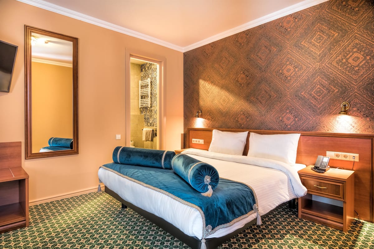 Ein Hotelzimmer mit einem großen Bett, einem Nachttisch mit Lampe, einem Kleiderschrank und einem Spiegel.