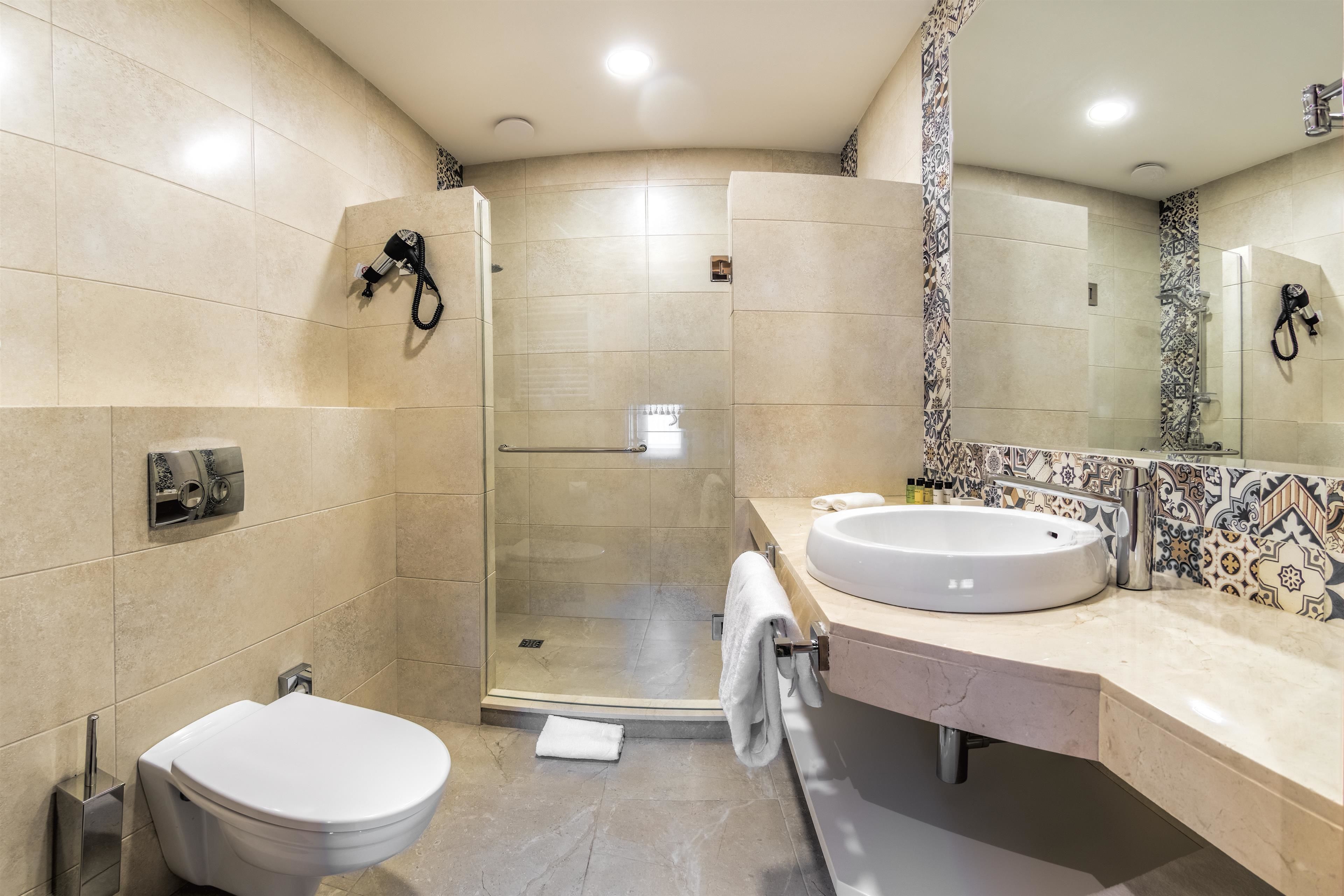 A modern bathroom with a glass-enclosed shower, a white toilet, and a large sink with a decorative tile backsplash.