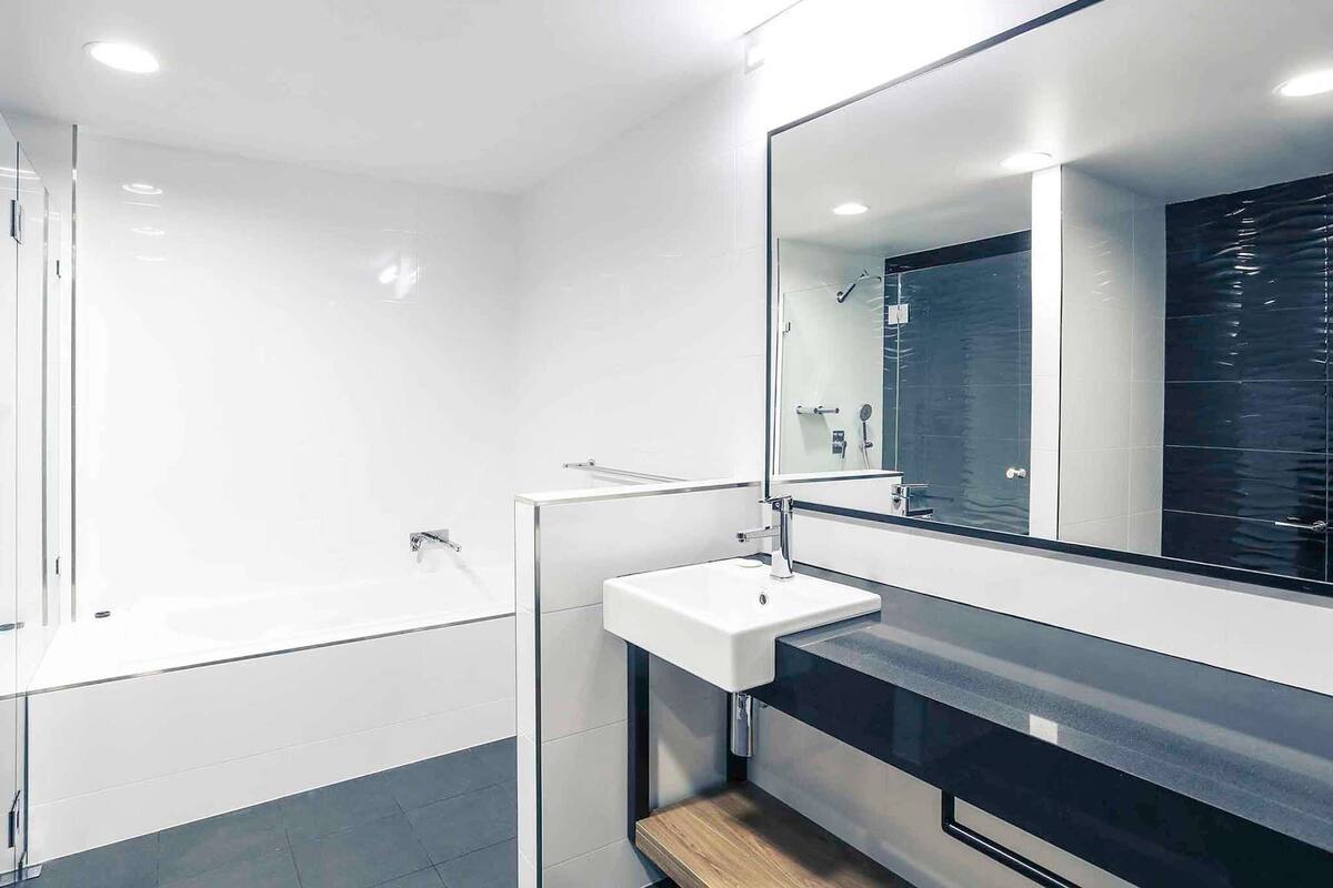 Een moderne badkamer met een douchecabine van glas, een wit wastafeltje en een grote spiegel.