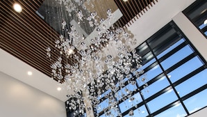 A modern interior with a large chandelier, a reception desk, and large windows offering a view of the outside. - Mercure Tamworth (West Tamworth)