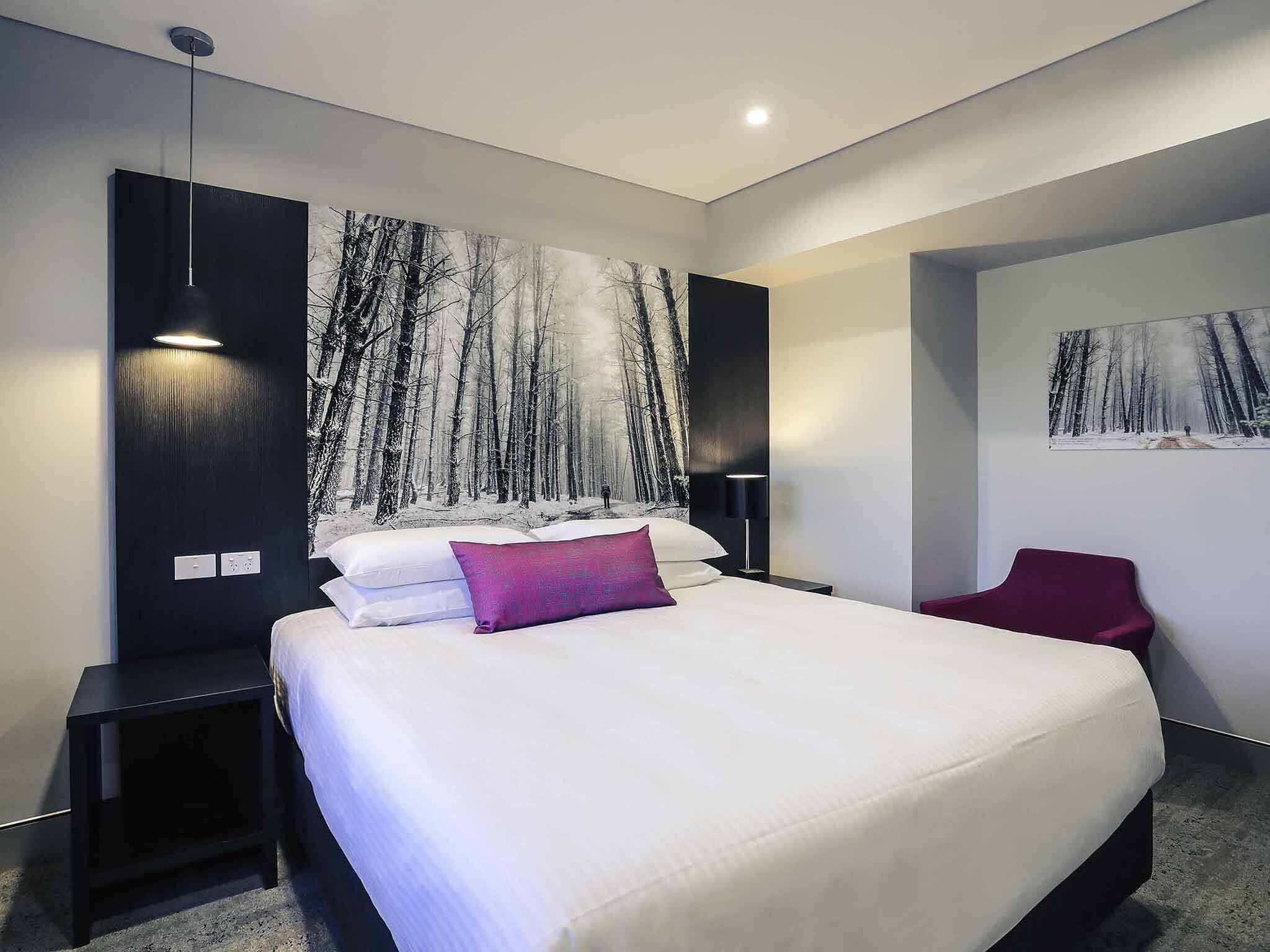 A modern bedroom with a large bed, a nightstand, a red chair, and a wall-mounted painting.