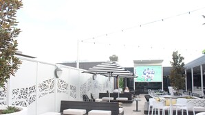 An outdoor seating area with white and black striped umbrellas, white and black patterned cushions, and a large screen displaying a sports event. - Mercure Tamworth (West Tamworth)