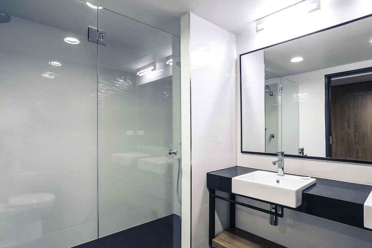 A modern bathroom with a glass shower enclosure, a white sink with a black countertop, and a large mirror.