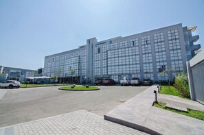 Un edificio moderno con una amplia fachada de vidrio, un patio central y un estacionamiento con varios autos.