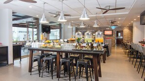 Un restaurante espacioso con una barra central, varios ventiladores de techo y diversas opciones de asientos, incluyendo taburetes y mesas.