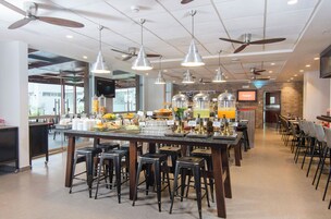 Un restaurante espacioso con una barra central, varios ventiladores de techo y diversas opciones de asientos, incluyendo taburetes y mesas.