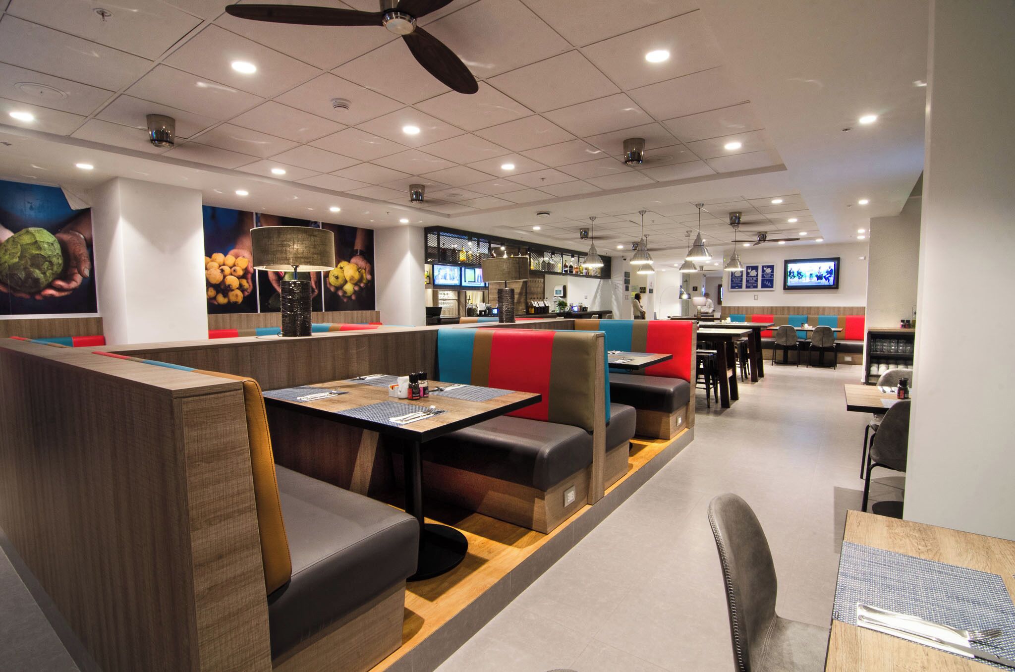 A modern restaurant with booths and tables, ceiling fans, and a bar area.