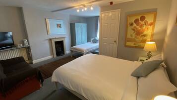 A hotel room with a bed, a desk, a television, a fireplace, and a painting.